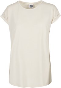 T-shirt corto a maniche corte di un leggero beige, realizzato in tessuto morbido, con scollatura rotonda e vestibilità rilassata, maniche arrotolate e spacchi laterali.