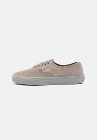 Basket basse beige en daim de Vans avec fermeture à lacets et semelle en caoutchouc blanc, vue du côté extérieur sur un fond blanc.