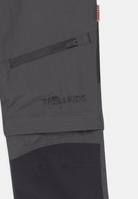 Grijze buitenbroek met een donkergrijze accenten, uitgerust met een ritszak en het "TROLLKIDS" logo gestikt in donkere draad.