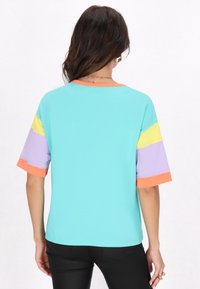 Top a maniche corte con corpo aqua, maniche colorate in blocchi giallo, lavanda e arancione, scollatura tonda e superficie liscia.