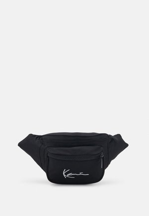 Riñonera de tela negra con dos compartimentos con cremallera y un logo en letra blanca en el bolsillo delantero, sobre un fondo liso.