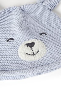 Pletená modrá čepice s ušima, huňatou bílou tváří medvěda, černými vyšitými detaily a měkkým texturovaným povrchem.