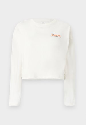 Bijela dugačka majica s dugim rukavima skraćena, napravljena od meke tkanine, s narančastim logotipom na lijevoj strani prsnog koša i opuštenim krojem sa ravnim rubom.