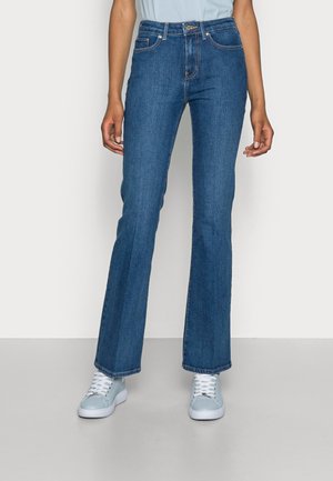 Mørkeblå flared jeans lavet af denim, med høj talje, fem lomme stil og synlige sømdetaljer, parret med lyseblå sneakers.