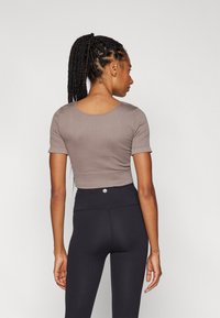 Fitted kortmouwtop in taupe geribbeld stof, met een ronde halslijn en cropped ontwerp, gecombineerd met zwarte high-waisted legging.
