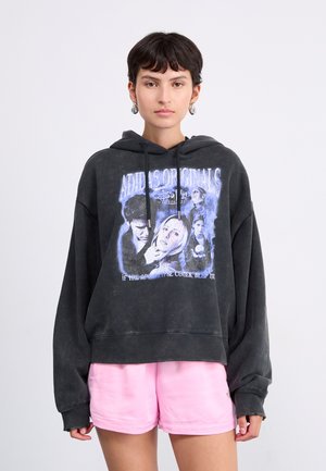 Hoodie surdimensionné noir en coton, avec un imprimé graphique et des accents bleus. Associé à un short rose clair.