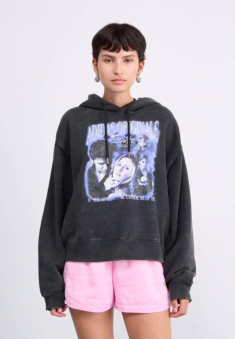 Felpa nera oversized in cotone con una stampa grafica e dettagli blu. Abbinata a pantaloni corti rosa chiaro.