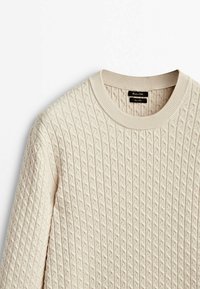 Beige gestrickter Pullover mit einem strukturierten Rautenmuster, Rundhalsausschnitt und gerippten Kanten. Etikett im Kragen sichtbar.