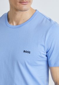 Lyseblå t-skjorte i bomull med rund hals og korte ermer. Har en diskré svart "BOSS"-logo på brystet. Glatt tekstur.