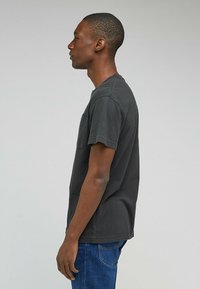 Svart bomull T-shirt med korta ärmar, rund hals och en vänster bröstficka. Den har en avslappnad passform och subtil textur.