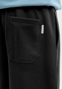 Sorte sweatpants lavet af blødt materiale med en rektangulær baglomme og et lille mærke på siden. Enkelt og funktionelt design.