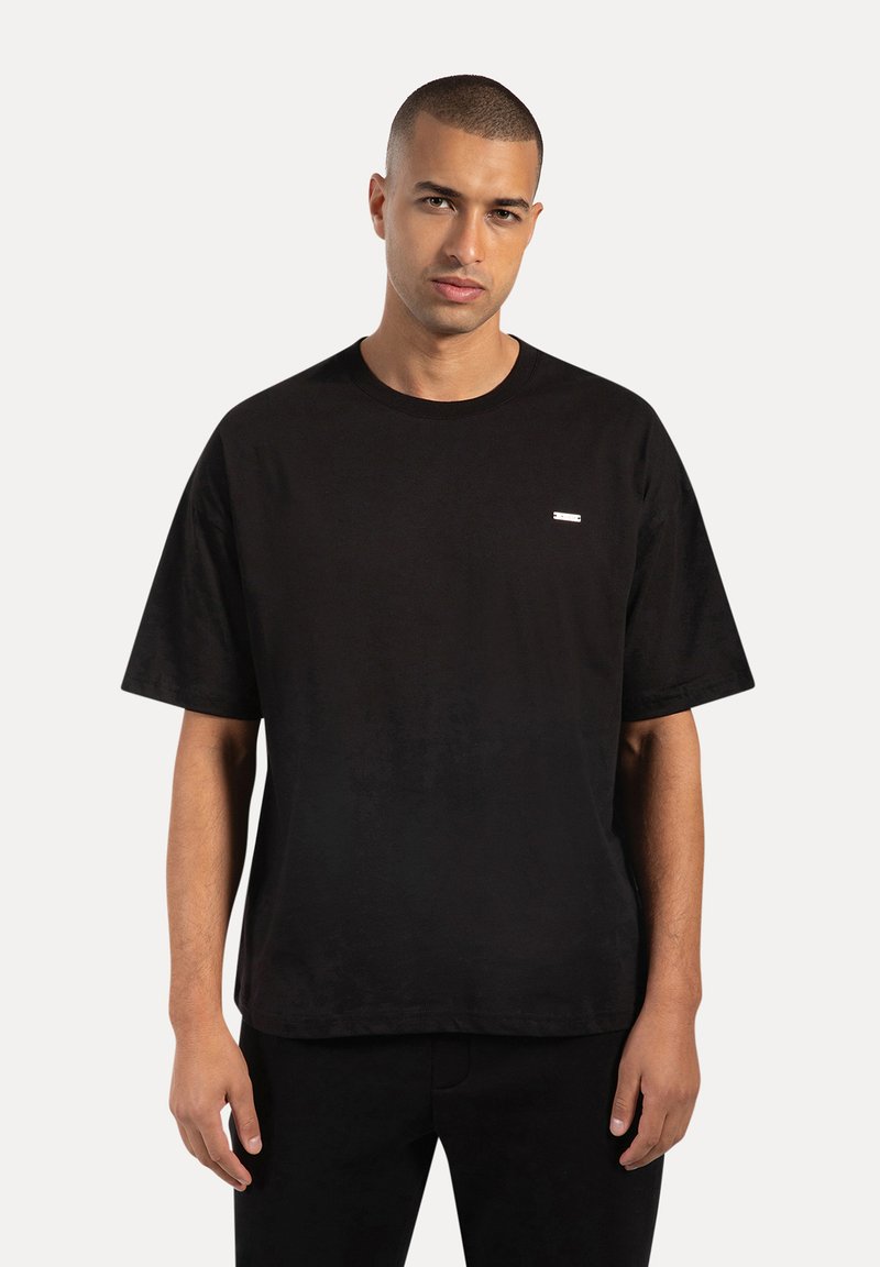 T-shirt in cotone nero con collo rotondo e maniche corte, caratterizzato da un piccolo etichetta rettangolare bianca sul lato sinistro del petto.