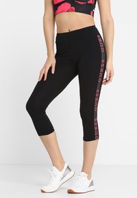 Leggings capri neri in tessuto elasticizzato con vita alta. Presentano dettagli con logo rosa sul lato e una texture liscia e elegante.