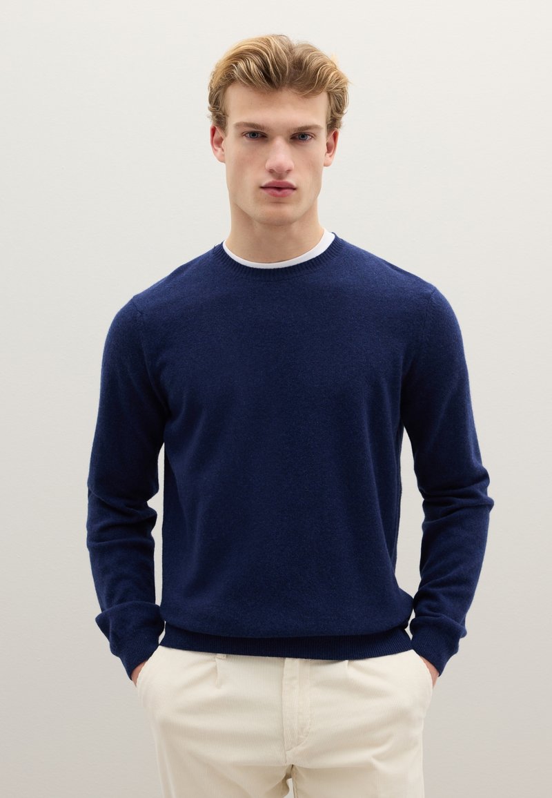 Maglione lavorato a maglia blu navy con maniche lunghe e scollo rotondo. Tessuto morbido, design aderente, abbinato a pantaloni di colore chiaro.