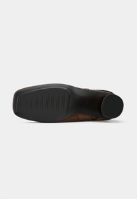 Suela de zapato de cuero sintético marrón con un diseño texturizado. Suela exterior de goma negra plana con surcos y un acento circular cerca del talón.