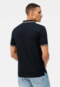 Polo shirt navy con maniche corte, caratterizzato da un colletto a costine con strisce verdi, bianche e gialle, e orlo dritto.