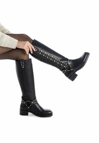 Botas de cuero negras hasta la rodilla con un tacón grueso, con remaches y hebillas de plata en el lateral para añadir detalle. Textura suave, diseño elegante.