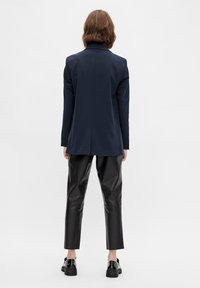 Navy blue tailored blazer with a single vent, paired with shiny black leather cropped pants and black lace-up shoes.