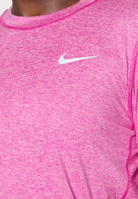 Vaaleanpunainen urheilupaita, jossa on kirjailtu pinta, pyöreä kaula-aukko ja valkoinen Nike-logo vasemmassa yläkulmassa.