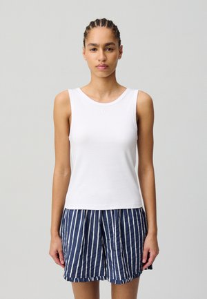 Canottiera bianca con scollo a barca, indossata con pantaloni corti a righe blu navy e bianchi, caratterizzati da una vestibilità rilassata e un tessuto leggero.