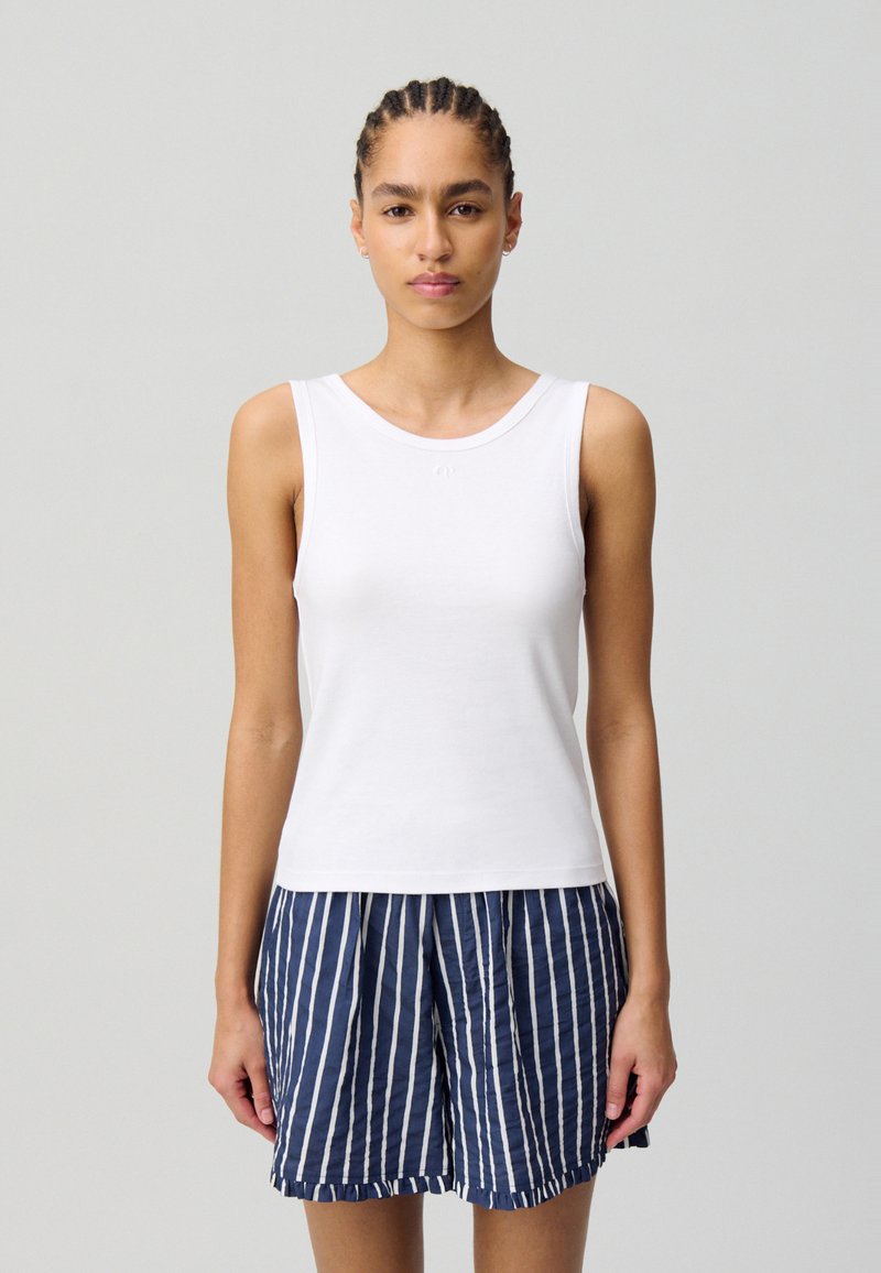 Top sin mangas blanco con escote redondeado, combinado con pantalones cortos a rayas en azul marino y blanco, que presentan un corte holgado y una tela ligera.