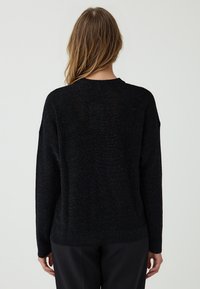 Maglione nero a maglia con scollatura rotonda, maniche lunghe, vestibilità morbida e finitura testurizzata. Nessun motivo o accessorio visibile.