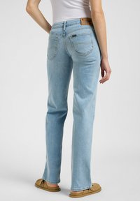 Jeans de denim azul claro con un diseño de pierna recta, bolsillos traseros visibles y una etiqueta de cuero marrón en la cintura. Textura suave.