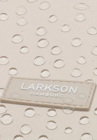 Tessuto beige con gocce d'acqua in rilievo e un'etichetta logo Larkson Hamburg in grigio chiaro, caratterizzato da una forma e una texture rettangolari.