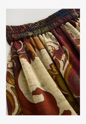 Patterned skirt featuring a smocked waistband, vibrant floral designs in red, yellow, and green on a cream background. Soft, draping fabric.