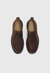 Pantofi din suede maro cu un design elegant, având o finisare netedă, vârf rotund și o talpă din cauciuc negru în contrast, cu accente de șireturi.