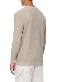 Maglione beige in maglia con un motivo tessuto e testurizzato. Presenta un collo rotondo e maniche lunghe. Dettaglio del logo piccolo vicino all'orlo.