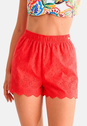 Shorts rouges taille haute avec broderie florale ajourée et ourlet festonné, associés à un haut court floral coloré.