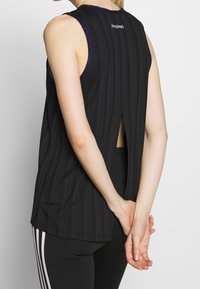 Haut sans manches noir avec un design à rayures texturées, col rond et une découpe dans le dos, rehaussé d'une bordure violette le long du cou.