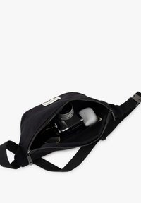 Black canvas bag with a zipper closure. Interior contains a camera, AirPods, and sunglasses. Features a padded strap for comfort.