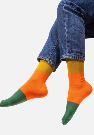 Kolorowe skarpetki w odcieniach pomarańczowego, zielonego i musztardowego, wykonane z gładkiego materiału, w standardowym fasonie sięgającym do kostki.