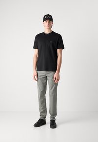 Černé tričko a světlé šedé kalhoty. Tričko má malé logo a outfit doplňují černé tenisky a černá kšiltovka.