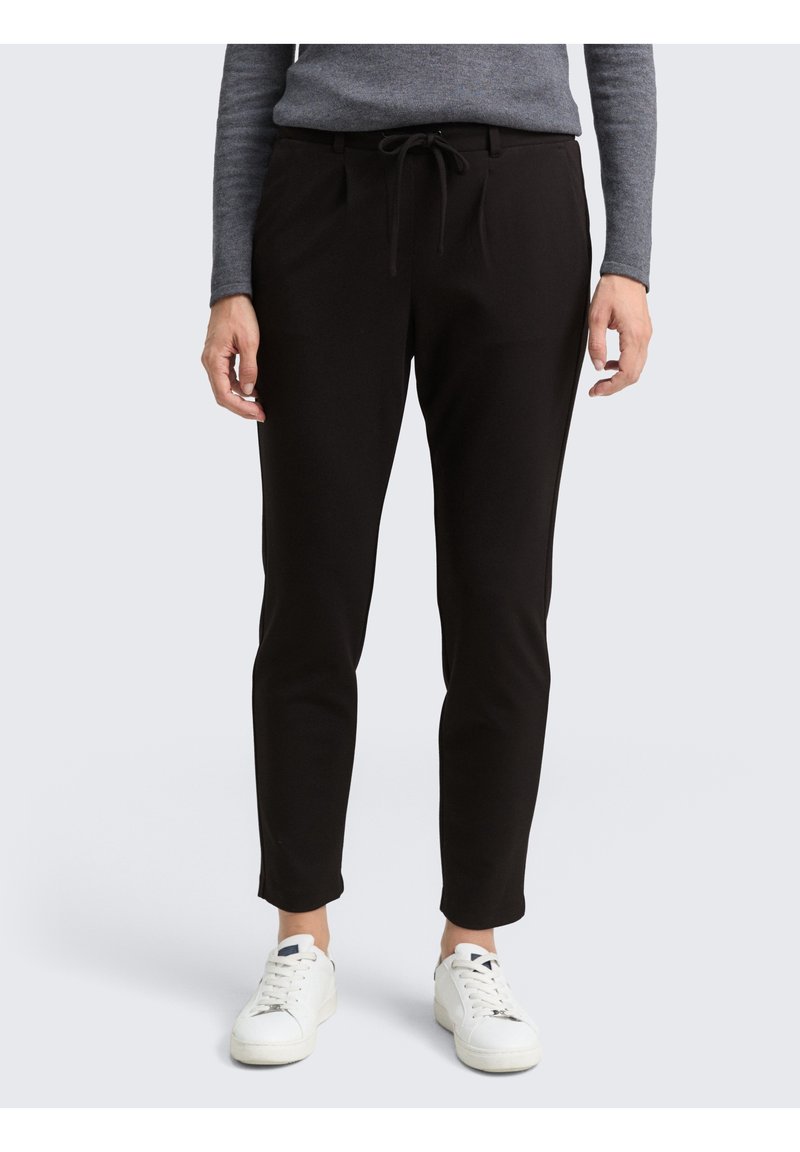 Pantaloni neri a vestibilità slim, realizzati in materiale morbido, con cintura elasticizzata e tasche laterali. Indossati con sneaker bianche.