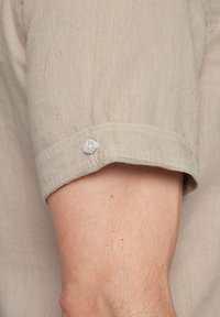 Licht beige linnen overhemd met korte mouwen, voorzien van een opgerolde manchet en een wit kunststof knoopdetail. Zachte, gestructureerde stof en nette stiksels.