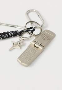 Porte-clés téléphone à clapet argenté avec bracelet tressé noir et blanc, breloque étoile en métal, et motif cœur texturé au dos.