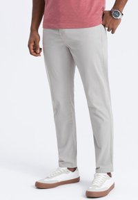 Pantalons chino gris clair à coupe slim, en coton, avec une texture subtile et des poches standard, associés à des baskets blanches et à une chemise rouge.