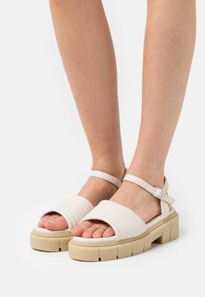 Sandalias de plataforma blancas con textura acanalada en la parte superior, correa ajustable en el tobillo y suela gruesa de color beige. Acabado suave y diseño sencillo.