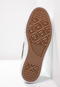 Semelle extérieure en caoutchouc marron avec motif géométrique, bordure latérale blanche et logo Converse. Surface texturée pour une meilleure adhérence, illustrant durabilité et design.