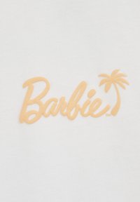 Tela blanca con un logo en relieve de "Barbie" en un suave color durazno, acompañado de un acento en forma de palmera. Textura suave con un diseño casual.