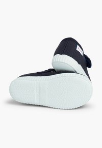 Tumesinised kangast tenniset, millel on tekstuuriga valge kummist tald, ümar varvas ja Velcro rihm, millel on suurus 23 ja "Valmistatud Hispaanias."