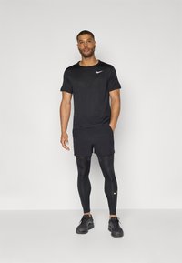 Black athletic t-shirt with short sleeves and a small white Nike logo, paired with black shorts and black leggings. Black athletic shoes.