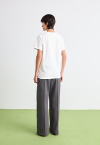 T-shirt blanc à manches courtes avec une coupe droite et une couture horizontale au dos, associé à un pantalon large gris taille haute.