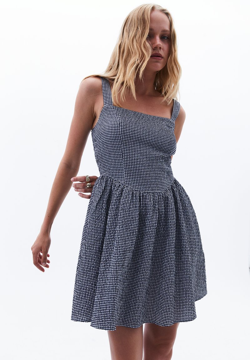 Neliökauluksellinen mekko, jossa on tummansininen ja valkoinen ruudullinen kuvio, varustettuna istuvalla yläosalla ja levenevällä hameella, valmistettu kevyestä kankaasta.