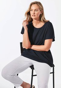 Zwart top met korte mouwen en een ronde hals, gecombineerd met lichtgrijze broek tot de enkels. Glad materiaal, ontspannen pasvorm, minimalistisch design.
