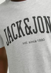 Camiseta de algodón gris con letras negras en negrita "JACK & JONES" y "intl. desde 1990" en el frente, con un diseño de cuello redondo.