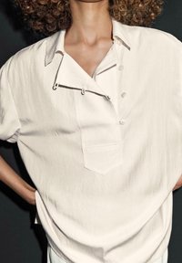 Lichtbeige kortekorte mouwenshirt met een button-up kraag, borstzak en decoratieve lus details, gemaakt van een textuur, lichtgewicht stof.